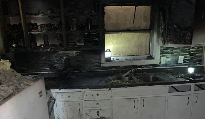 Kitchen interior showing severe fire and smoke damage on walls and appliances
