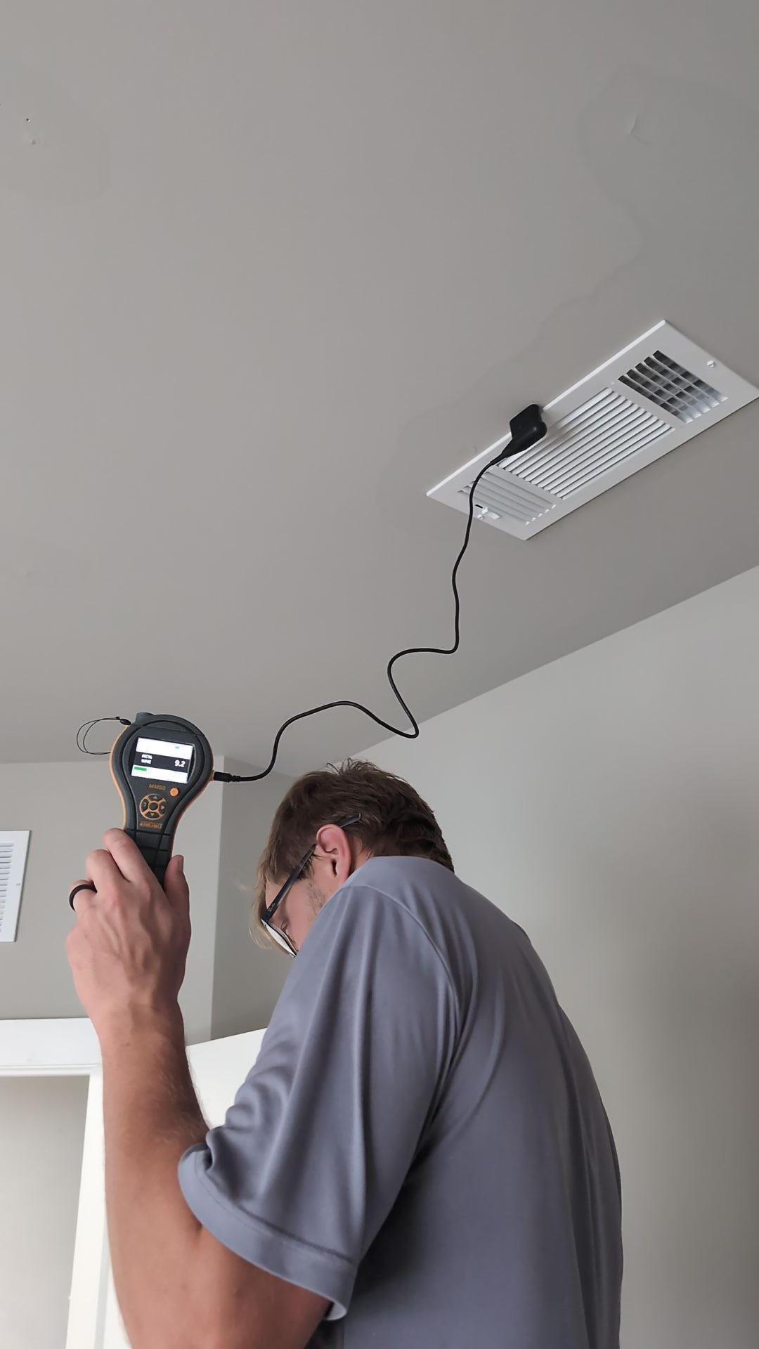 A technician uses a moisture meter with a specialized probe to assess water damage and detect hidden moisture within a ceiling vent after a roof leak. This professional ceiling leak detection and moisture assessment is critical for planning a comprehensive water damage restoration solution.