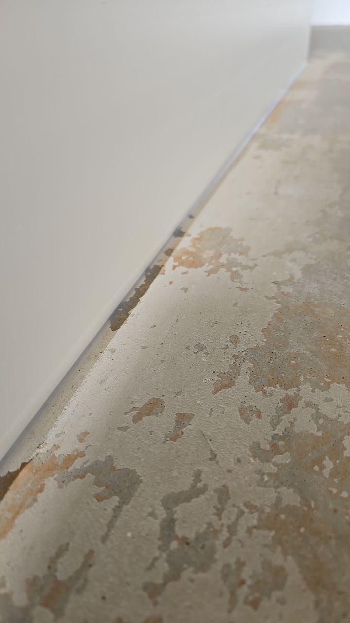 A close-up of water damage on a concrete floor and baseboard caused by water intrusion from a roof leak. Our water damage restoration team quickly began the cleanup process to mitigate damage and prevent mold growth, a key step in a full property restoration.