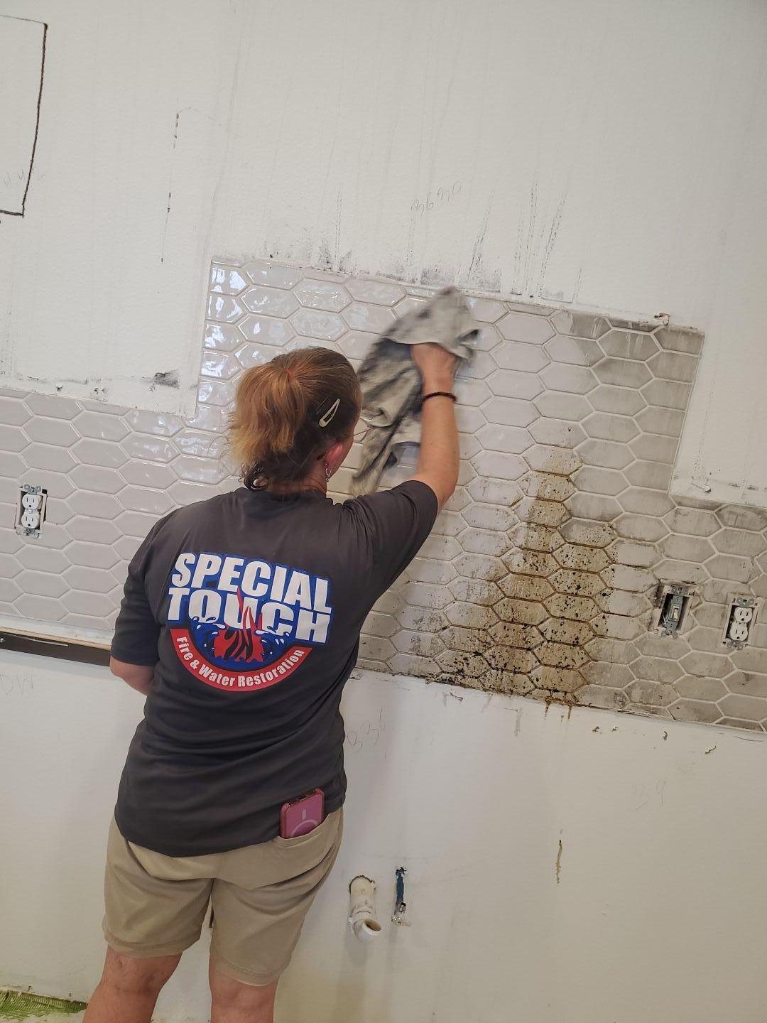 Our team member meticulously cleaning soot and smoke residue from kitchen tiles after a fire. This detailed fire damage cleanup is essential for removing lingering odors and restoring the property to a safe and clean condition, a key part of our property restoration services that also address related water damage.