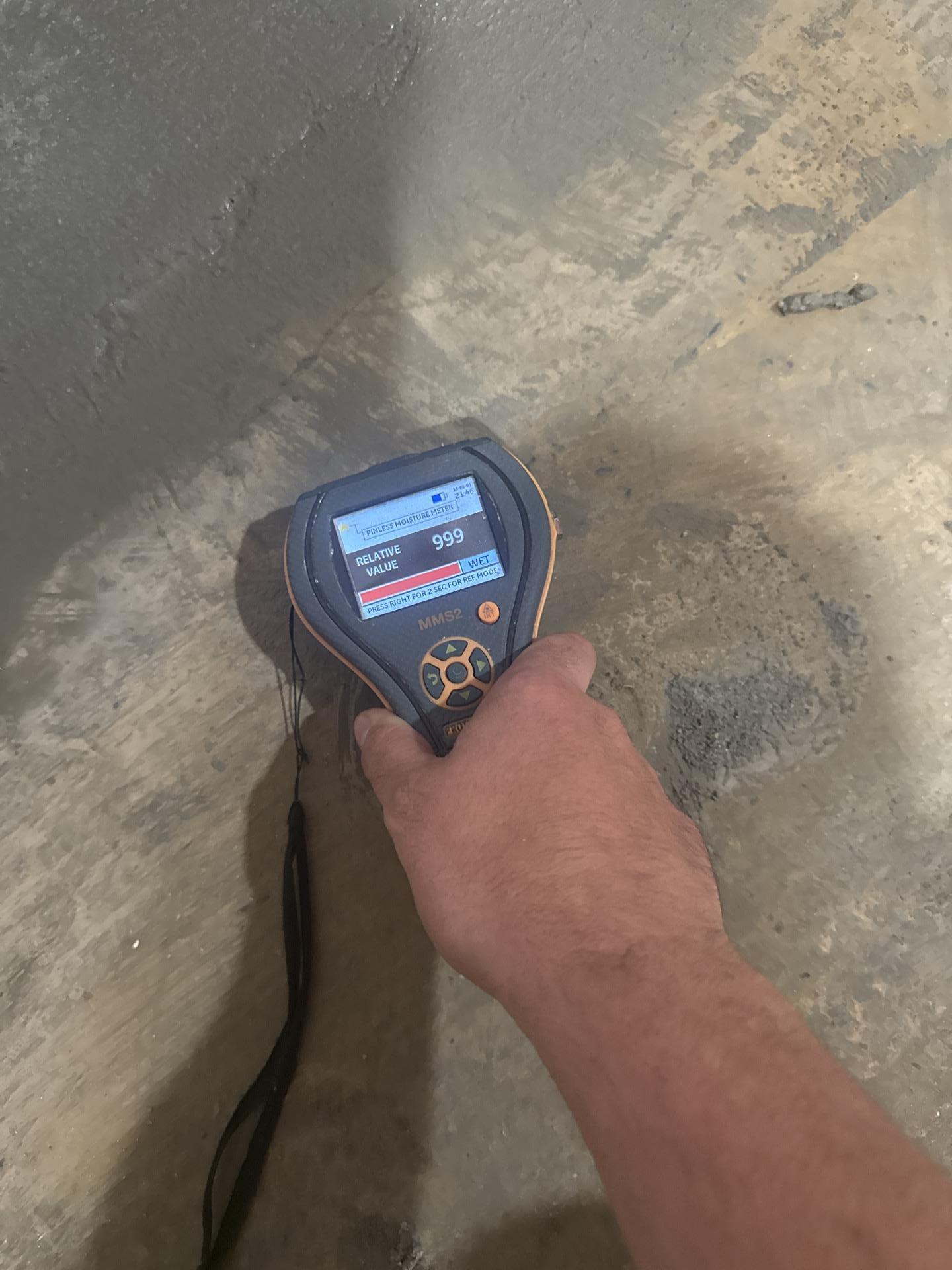 A professional uses a moisture meter to detect a high level of concrete water damage after a busted line. This is a critical step in our water damage restoration process to accurately assess the extent of the damage and plan for effective repairs and cleanup