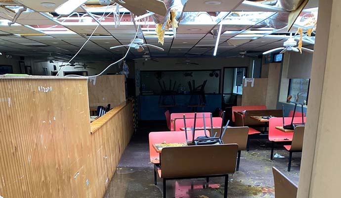 Restaurant interior with damaged ceiling and exposed insulation Restaurant interior with collapsed ceiling, wet floors and overturned furniture after a disaster