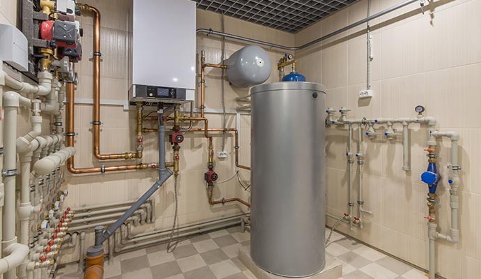 Large water heater tank with pipes, valves and gauges Large water heater tank surrounded by pipes, valves, gauges and control units in a utility setup