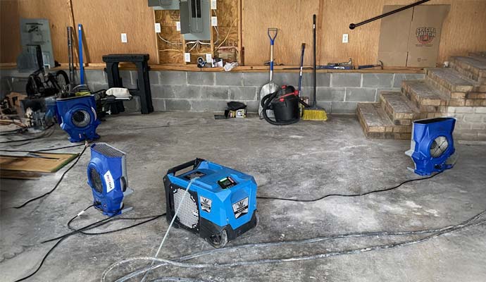 Workers using equipment to restore a basement floor damaged by water.